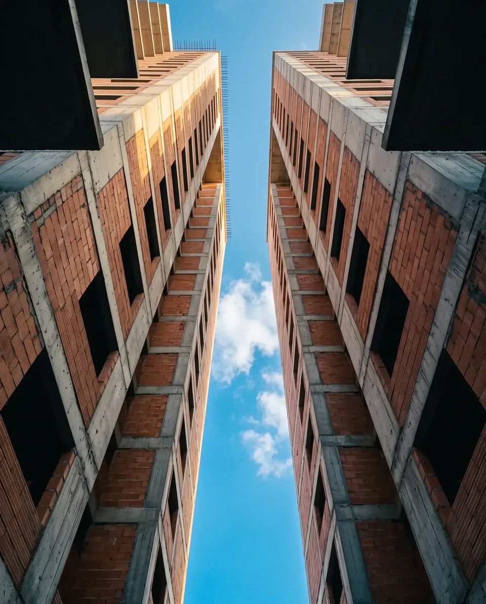 Dois prédios de blocos cerâmicos vistos de baixo, com uma faixa de céu entre eles