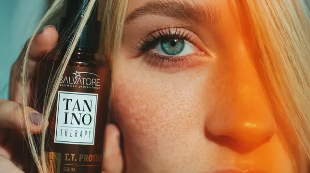 Mulher loira segurando o produto Tanino Therapy da HD Cosméticos junto ao rosto, em close